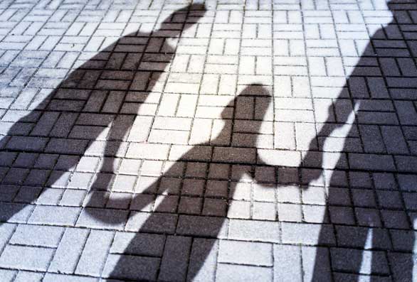 Shadows of parents and their child cast onto a brick sidewalk.